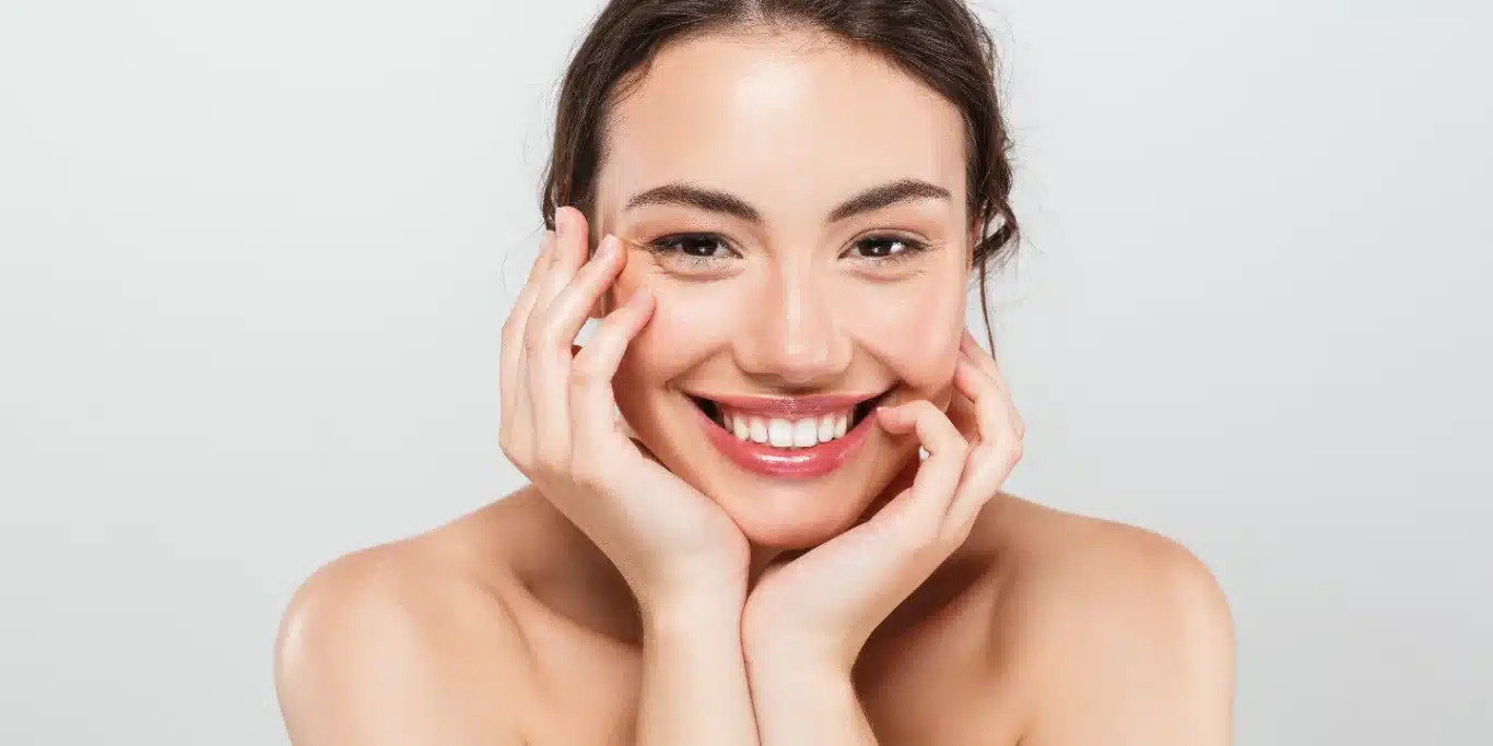 Smiling woman with clear skin touching her face.